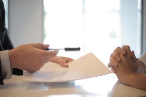 individu tendant une feuille et un stylo pour qu'un autre homme signe un contrat